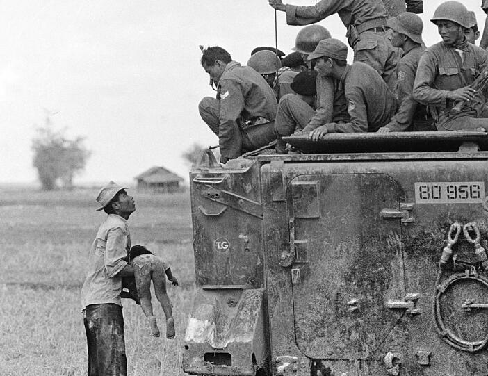 Ein Vater hält den Körper seines Kindes, während südvietnamesische Army Rangers von einem Tank herunterschauen. (März 1964). Das Kind wurde getötet, als Regierungstruppen Guerilla-Kämpfer in einem Dorf nahe der kambodschanischen Grenze verfolgt hatten.