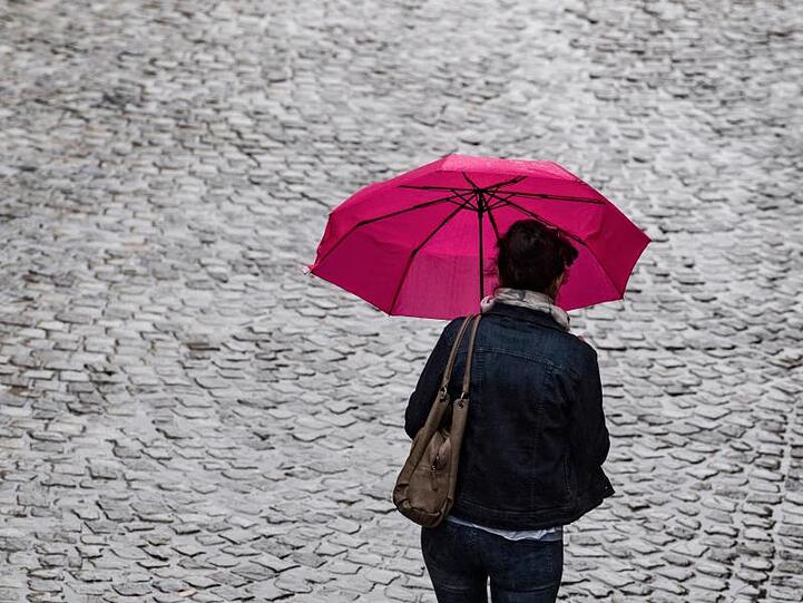 Ein Frau geht mit Regenschirm über eine Straße. Foto: Hendrik Schmidt/Archiv