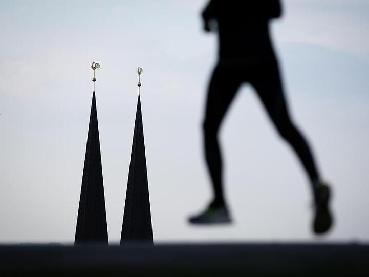 Eine Jogger läuft vor den Türmen einer Kirche. Foto: Friso Gentsch/dpa/Symbolbild