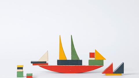 Auch das bunte Schiff gehört zu den Bauhaus-Hits. Es zeigt zudem gleich die pädagogischen Grundsätze der Kunstschule, nämlich die &bdquo;schöpferische Selbstbetätigung als Grundlage des elementaren Lebensausdrucks&ldquo;. Neben verschiedenen Kinderzimmermöbeln hat die Studentin Alma Buscher im Jahr 1923 das Schiffbauspiel in einer großen und einer kleinen Version entworfen. Buscher legte großen Wert auf harmonische Proportionen und klare Einzelteile, die Kinder nicht verwirren. Das Gelb, Blau oder Rot sollte auch die &bdquo;Farbfröhlichkeit&ldquo; und damit die &bdquo;Freudigkeit des Kindes&ldquo; steigern. Material wurde bei der Herstellung sparsam verwendet, das Schiff konnte man aus zwei Holzleisten sägen. Heute nennt man das nachhaltig.