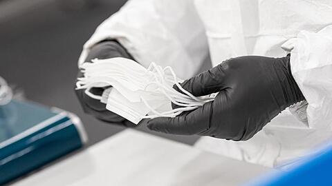 Ein Mitarbeiter prüft und stapelt in einem Werk zuvor gefertigte medizinische Masken.