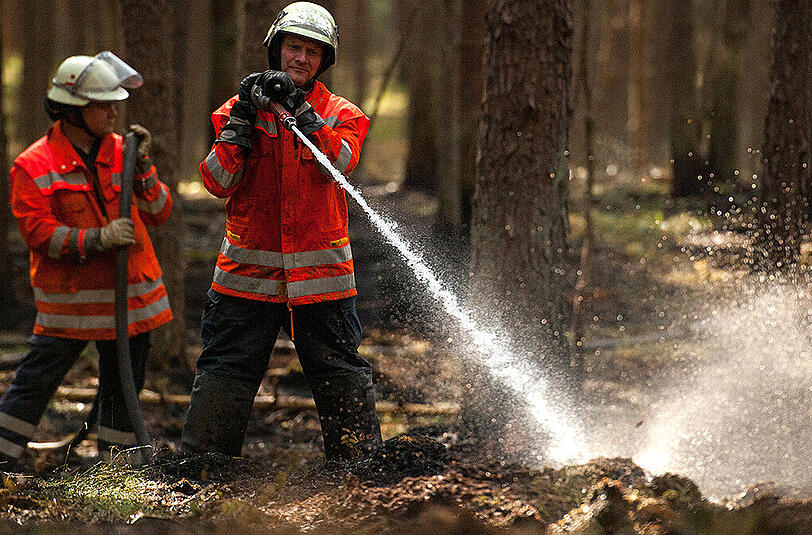 Einsatzkräfte der Feuerwehr führen Nachlöscharbeiten in einem Waldstück bei Mechtersen im Kreis Lüneburg nach einem Feuer im torfigen Boden durch.