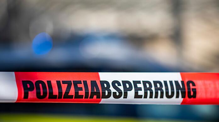 Ein Absperrband mit der Aufschrift "Polizeiabsperrung" ist vor einem Polizeiwagen aufgespannt.