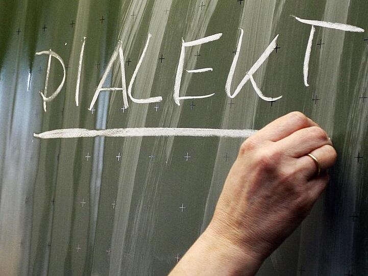 Eine Frau schreibt das Wort "Dialekt" auf eine Tafel. Foto: Daniel Karmann/Archiv