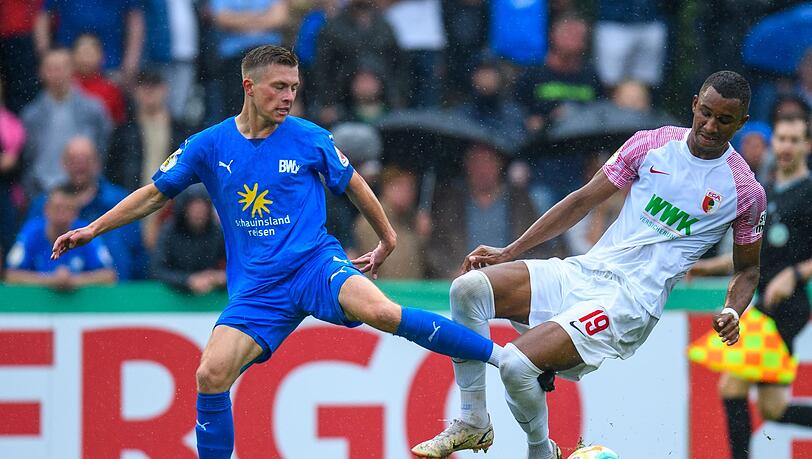 Lohnes Lennard Prüne (l) und Augsburgs Felix Uduokhai kämpfen um den Ball.