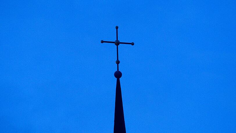 Das Kreuz einer Kirche ist in der Abenddämmerung zu sehen.