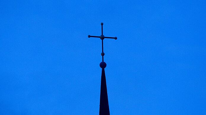 Das Kreuz einer Kirche ist in der Abenddämmerung zu sehen.