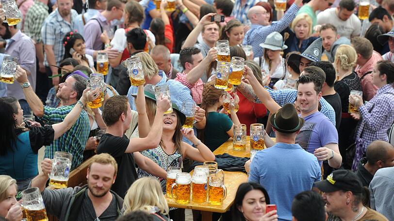 Besucher feiern auf dem Oktoberfest in einem der Festzelte und heben dabei ihre Bierkrüge.