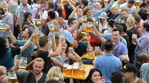 Besucher feiern auf dem Oktoberfest in einem der Festzelte und heben dabei ihre Bierkrüge.