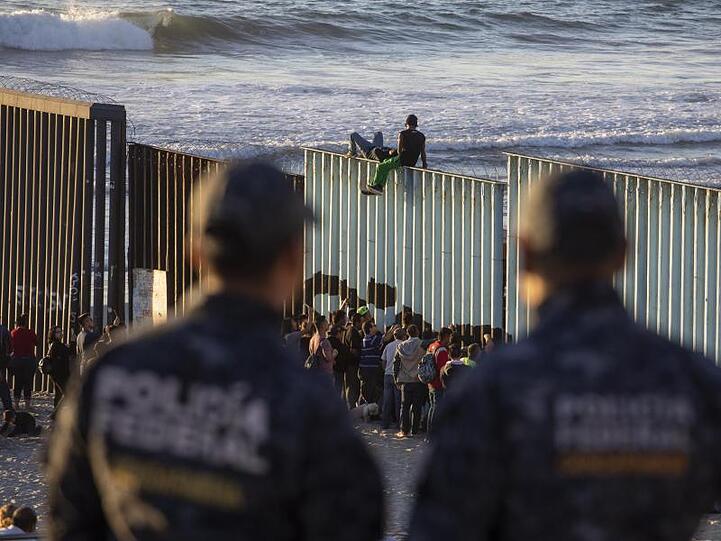 Zwei mexikanische Polizisten beobachten bei Tijuana Migranten am Grenzzaun zu den USA.