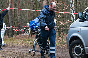 Mitarbeiter der Gerichtsmedizin bringen in einem Waldstück an der Bärenlauchstraße eine Leiche zu ihrem Fahrzeug.