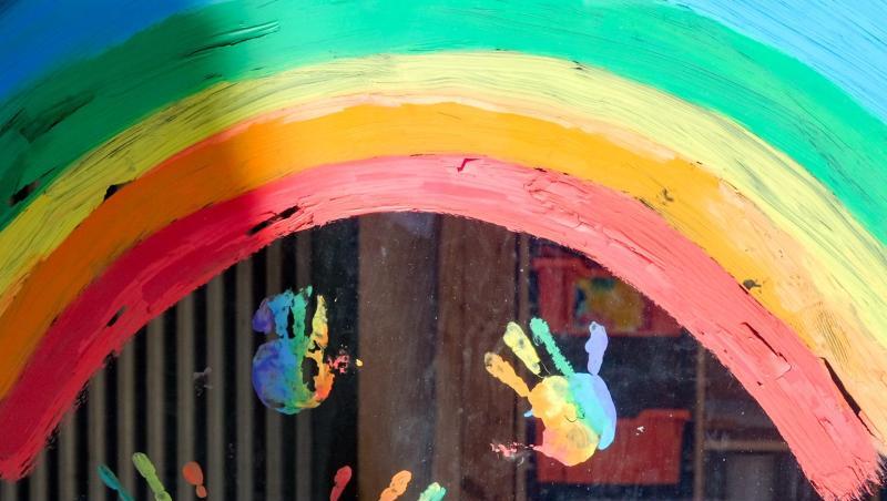 Kinderhände und ein Regenbogen sind an einer Kita zu sehen.
