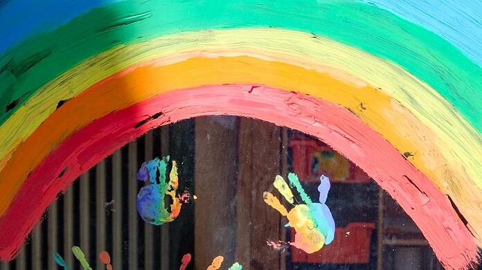 Kinderhände und ein Regenbogen sind an einer Kita zu sehen.