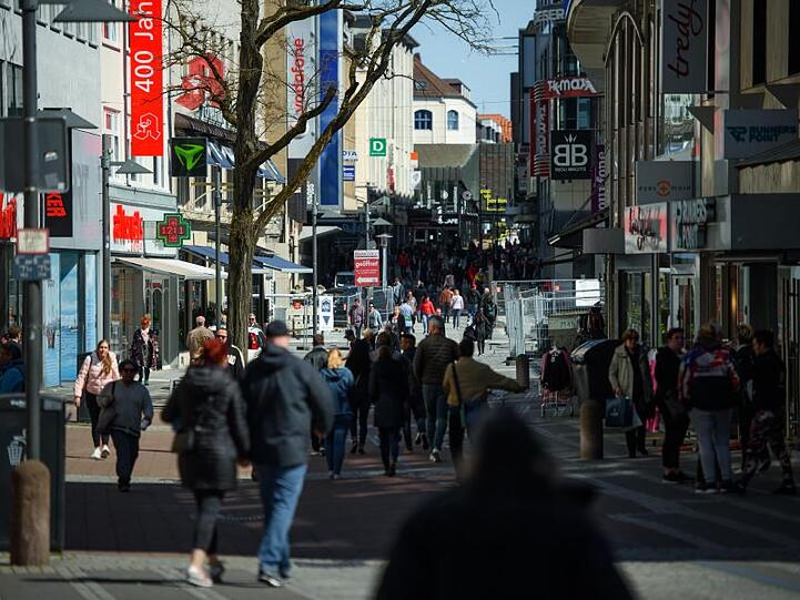Passanten gehen bei Sonnenschein durch eine Einkaufsstraße in einer Fußgängerzone. Foto: Gregor Fischer/dpa/Symbolbild