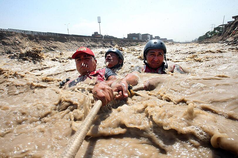 21.03.2017: Zwei Reservisten der peruanischen Armee und ein Zivilist halten sich in Lima (Peru) bei Rettungsarbeiten in einem überschwemmten Fluss an einem Seil fest.