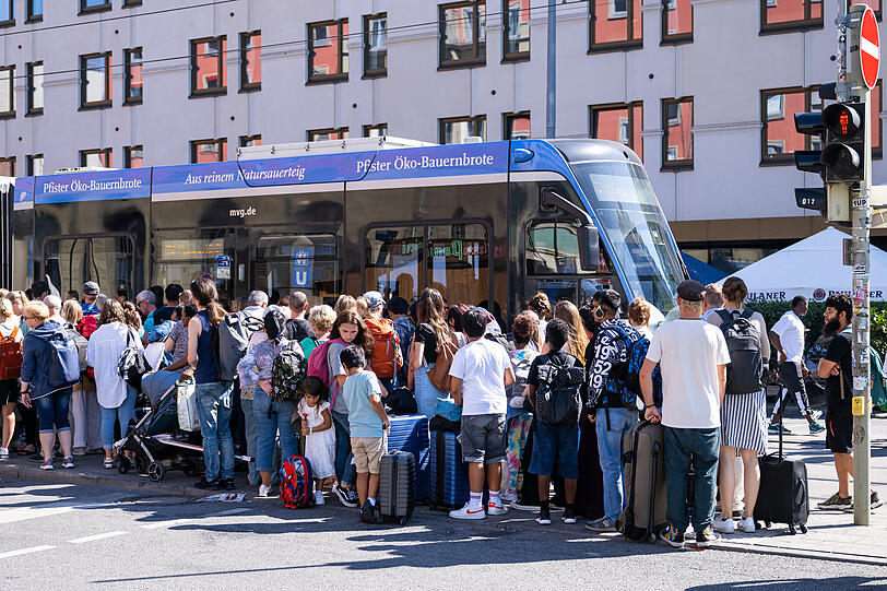 Reisende stehen vor dem Hauptbahnhof an einer Trambahn-Haltestelle.