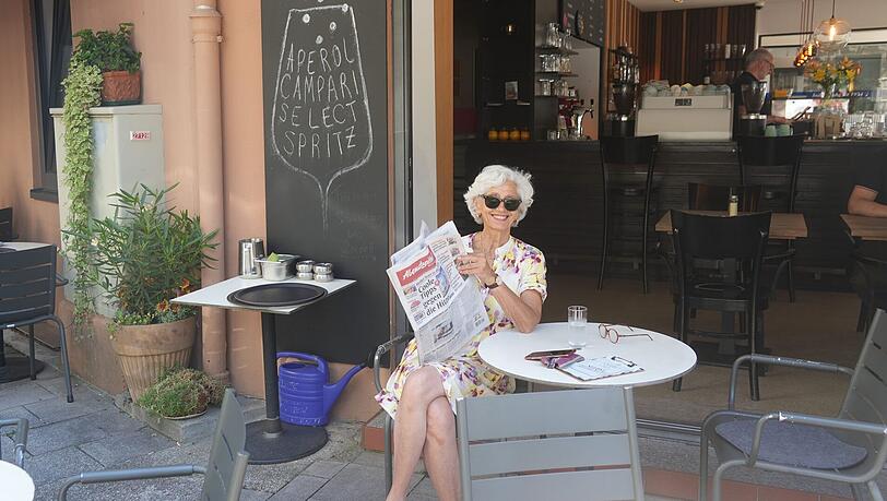Ein Platz im Schatten ist dieser Tage gold wert. Die App "SunnySites" hilft dabei, sie zu finden. Sabine genießt den Schatten draußen im Café Carl in der Clemensstraße und liest dabei die Abendzeitung.