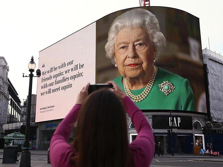 Ein Bild von Königin Elizabeth II. und Zitate aus ihrer Ansprache auf Anzeigetafeln am Piccadilly Circus in London.