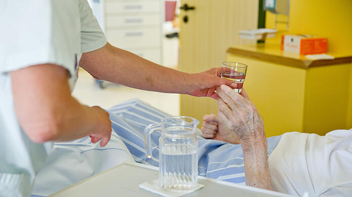 Eine Krankenpflegerin reicht einem Patienten ein Glas Wasser (Symbolbild).