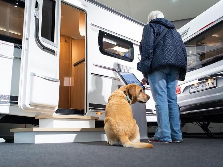 Ein Hund sitzt vor Wohnwägen auf der Reisemesse CMT. Foto: Tom Weller/dpa