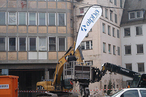 Alles bereit für den Fototermin: Der Abrissbagger mit dem Furcht einflößenden Greifer und die Fahnen von Gerd Schmelzers &bdquo;alpha&ldquo;-Immobilien-Gruppe.