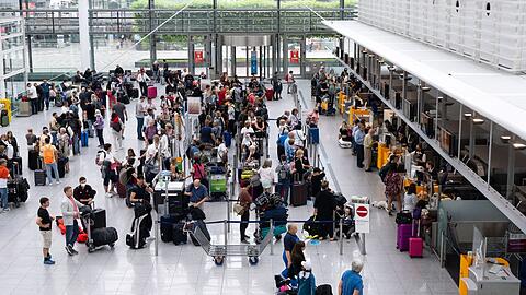 Passagiere stehen am Flughafen München an einem Check-in-Schalter.