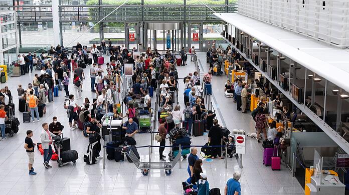Passagiere stehen am Flughafen München an einem Check-in-Schalter.