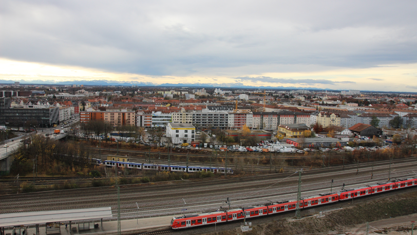 Aus dem Fenster kann man den Zügen nachschauen, im Hintergrund leuchten die Alpen.