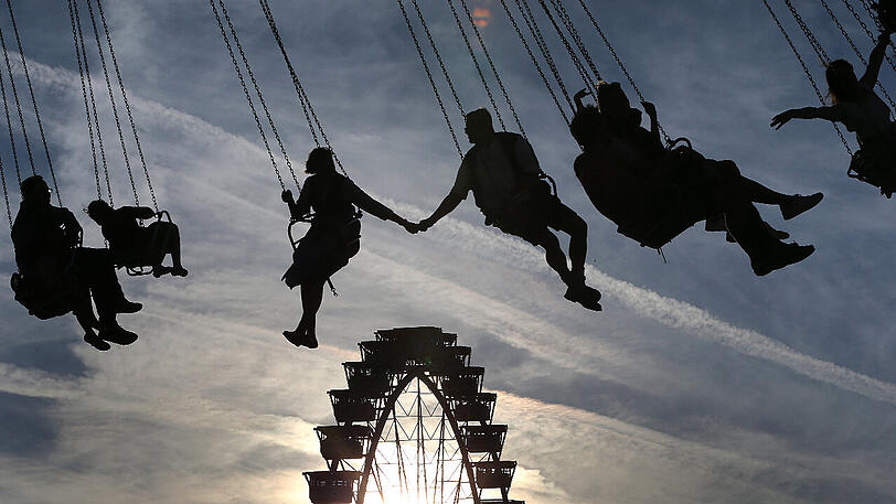 Wiesnbesucher fahren im Kettenkarussell vor dem Riesenrad.