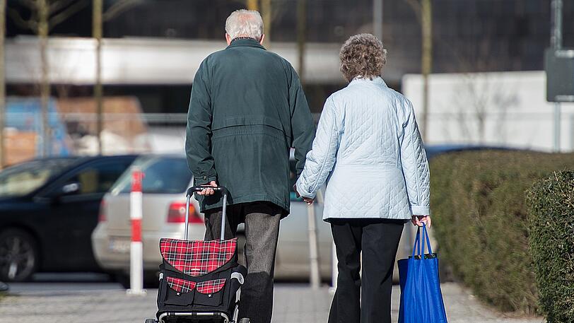 Ein älteres Paar geht mit Einkaufstrolley und -tasche durch die Straßen. (Symbolbild)