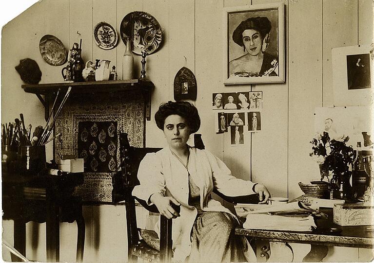 Olga Meerson lässt sich 1910 in ihrer Pariser Wohnung fotografieren, im Hintergrund hängt ihr Selbstbildnis.