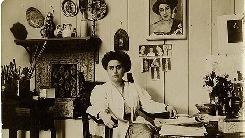 Olga Meerson lässt sich 1910 in ihrer Pariser Wohnung fotografieren, im Hintergrund hängt ihr Selbstbildnis.