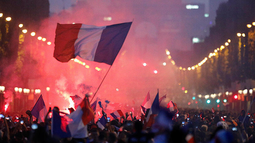 15.07.18: Fans von Frankreich feiern über den Sieg auf der Champs Elysees vor dem Arc de Triomphe und schwenken eine Nationalflagge.