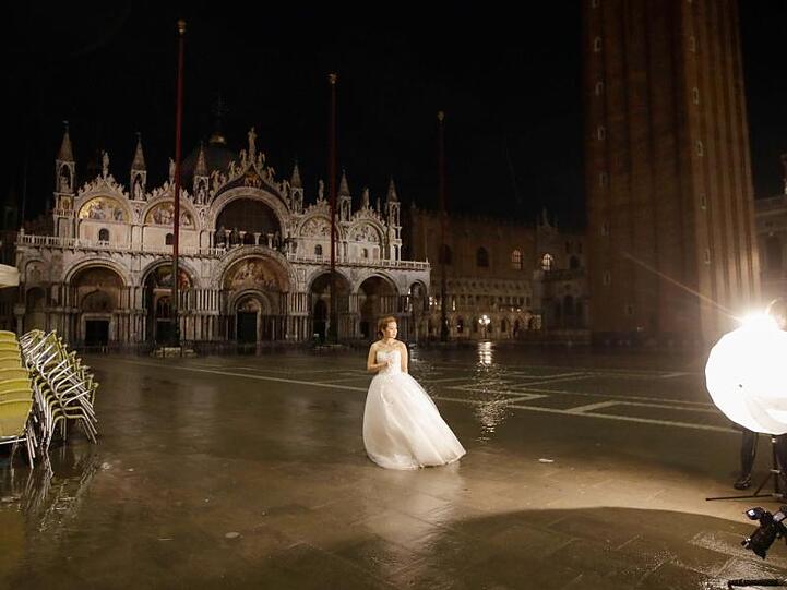 Fototermin: Eine Frau im Brautkleid steht am frühen Morgen auf dem überfluteten Markusplatz in Venedig.
