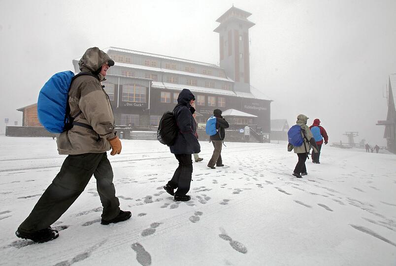 Wanderer laufen am Samstag durch Neuschnee vor dem Hotel Fichtelberghaus auf dem Gipfel des 1215 Meter hohen Fichtelbergs in Oberwiesenthal.
