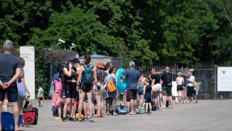 Menschen stehen bei warmem Wetter in einer Schlange vor dem Eingang zum Olympiabad in Berlin.
