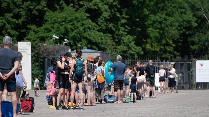 Menschen stehen bei warmem Wetter in einer Schlange vor dem Eingang zum Olympiabad in Berlin.