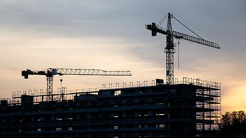 Kräne stehen hinter dem Rohbau für ein Bürogebäude auf einer Baustelle.