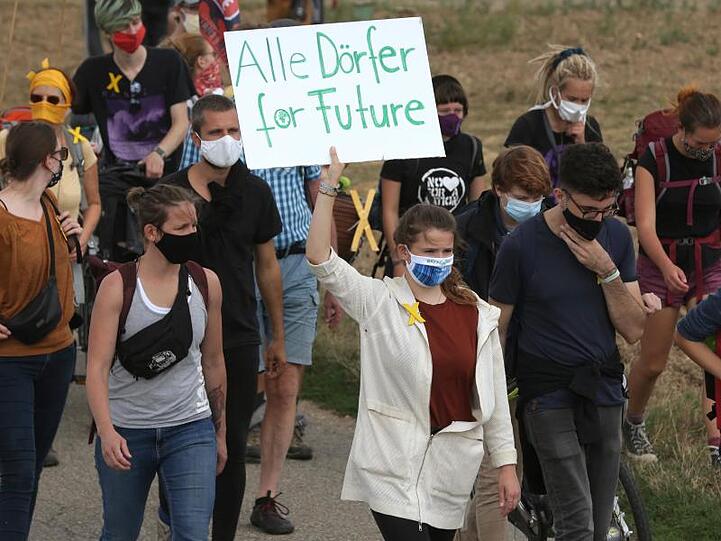 In dem Demonstrationszug aus Keyenberg zeigt Luisa Neubauer (M) ein Plakat mit der Aufschrift "Alle Dörfer for Future".