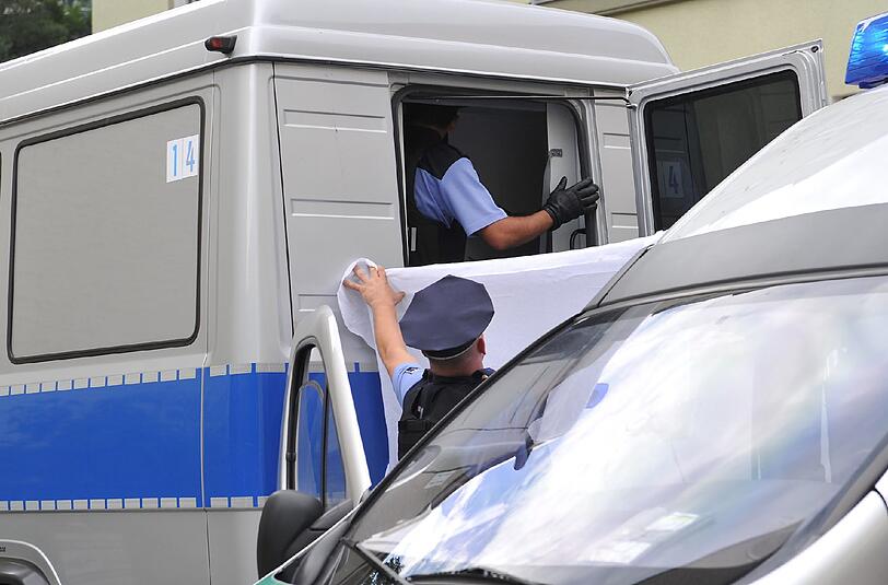 Verdeckt von einem weißen Tuch geleiten Polizisten am 12.8.2013 einen Verdächtigen aus dem Haus, in dem der Steuerberater erschossen wurde.