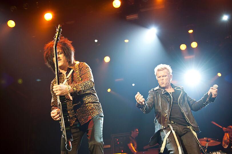Steve Stevens, Gitarrist und Begleiter seit den ersten Tagen, und Billy Idol, der selbst auf der schwülsten Bühne sein Konzert in vollem Ornat beginnt.