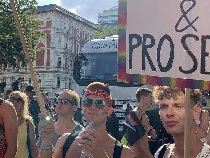 Teilnehmer einer CSD-Parade halten ein Plakat mit der Aufschrift "Pro Homo & Pro Secco" und eine Regenbogenfahne. Foto: Alexander Blum/dpa/Archivbild