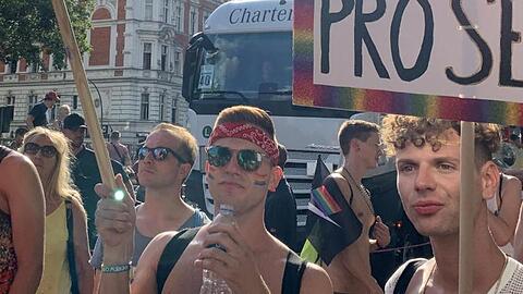 Teilnehmer einer CSD-Parade halten ein Plakat mit der Aufschrift "Pro Homo & Pro Secco" und eine Regenbogenfahne. Foto: Alexander Blum/dpa/Archivbild