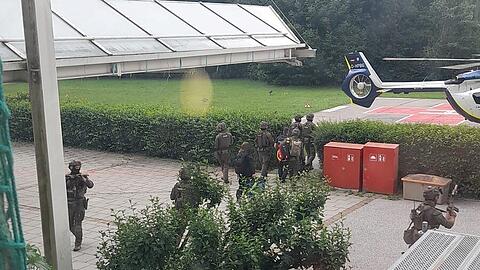 Beamte eines Spezialeinsatzkommandos bringen den 49-J&auml;hrigen in Fu&szlig;fesseln zu einem Polizeihubschrauber.