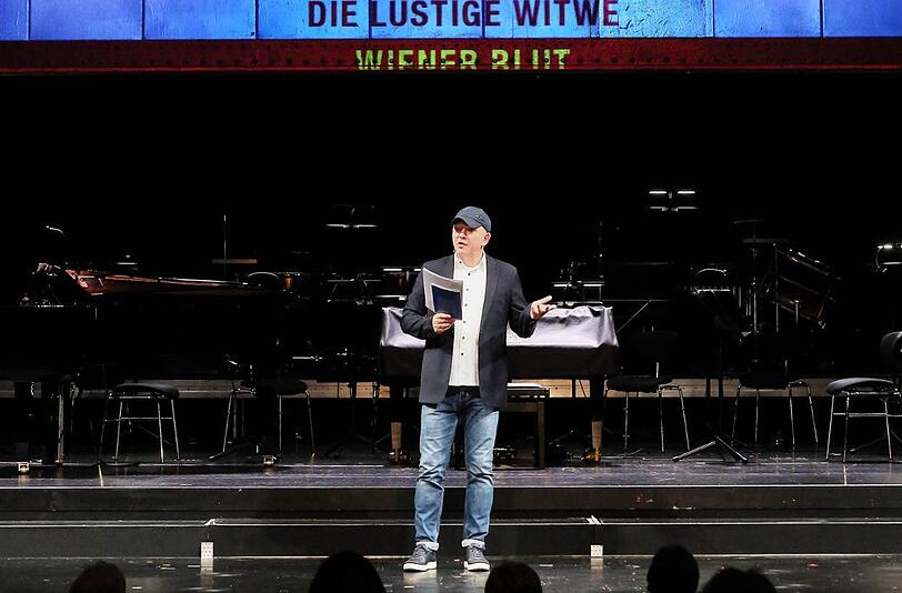 Josef E. Köpplinger, der Intendant des Gärtnerplatztheaters, bei der Vorstellung des Spielplans auf der Bühne. Über ihm eine Projektion mit Titeln aus dem Repertoire.
