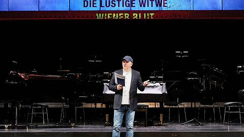 Josef E. Köpplinger, der Intendant des Gärtnerplatztheaters, bei der Vorstellung des Spielplans auf der Bühne. Über ihm eine Projektion mit Titeln aus dem Repertoire.