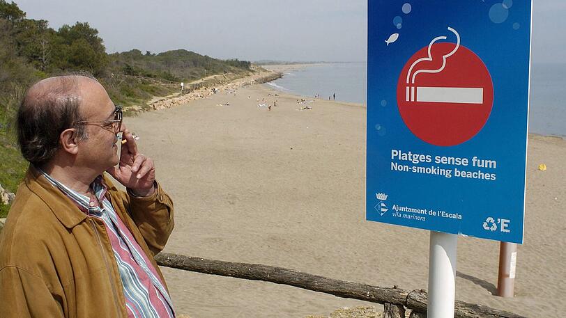 Ein Mann raucht, während er die Aufschrift auf einem Schild am Strand von l'Escala bei Girona im Nordosten Spaniens liest. Auf dem Schild steht geschrieben: «Nichtraucher-Strände». Kippen an Stränden sind in Spanien weiterhin unerwünscht.