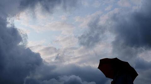 Ein Mann geht mit einem Regenschirm vor aufziehenden dunklen Wolken spazieren. Foto: Martin Gerten/Archivbild