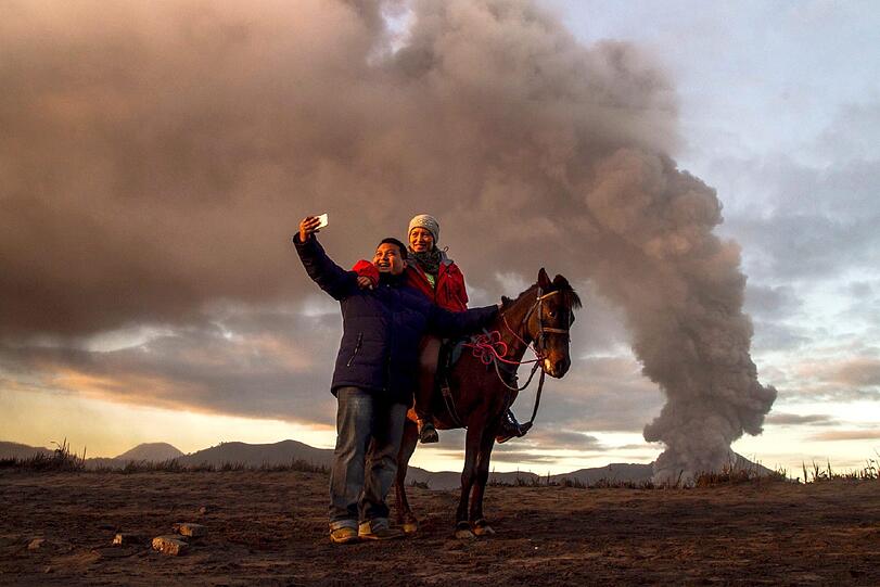 Touristen schießen ein Selfie vor dem indonesischen Mount Bromo in Probolinggo. Der Vulkan hat in den letzten Tagen vermehrte Aktivitäten gezeigt und ist auf der 2ten von vier Alarmstufen.