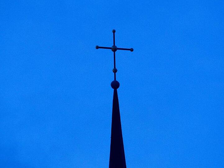Ein Kreuz ragt auf einer Kirche in den Himmel. Foto: Friso Gentsch/dpa/Archivbild